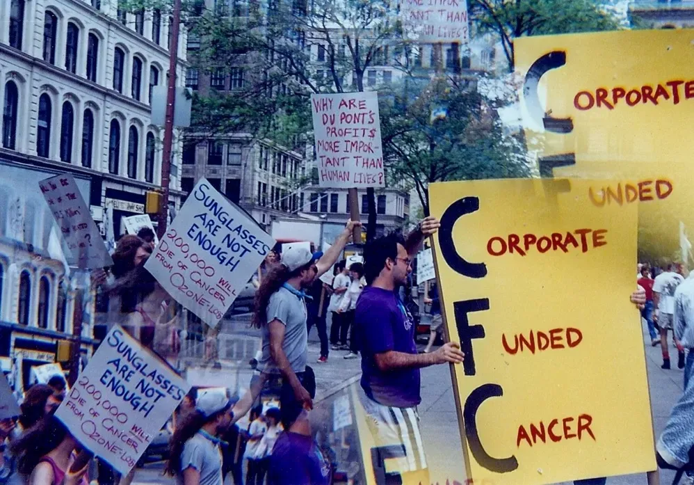 發生在紐約曼哈頓的一次保護臭氧層抗議，時間大約是上世紀八十年代末。標語牌上寫著：「光靠墨鏡是不夠的，臭氧層缺失將導致二十萬人死於癌症」，「為什麼杜邦公司的利潤比人命更重要？」，「氟氯化碳（CFC）=企業（Corporate）資助的（Funded）癌症（Cancer）」。（圖片來源：amNY）